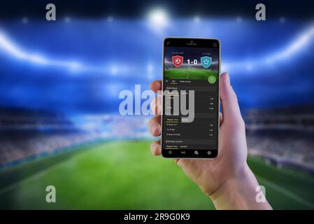 Online-App für Fußballwetten auf Smartphones, d. h. man Hand mit Fußballstadion im Hintergrund Stockfoto