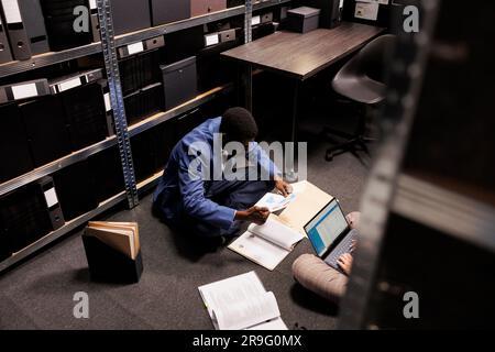 Ein afroamerikanischer Inspektor, der nach Hinweisen sucht, Beweise für den Tatort im Vorraum analysiert. Diverse Privatdetektive, die Überstunden bei der Kriminalermittlung machen. Strafverfolgungskonzept Stockfoto