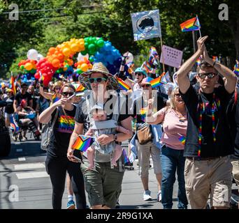 Foto eines Paradeteilnehmers mit der Progress Pride-Flagge und dem Baby, das während der jährlichen Pride-Parade der Stadt vor sich trägt. Stockfoto