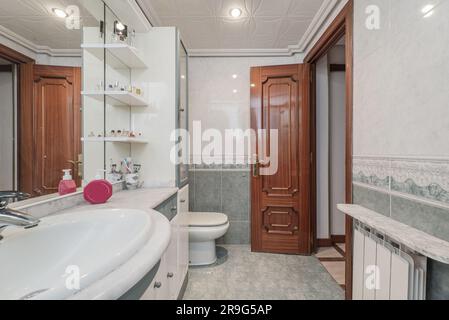 Herkömmliche Toilette mit weißen und grünen Holzmöbeln mit Porzellanwaschbecken, eingebettet in eine Marmorablage unter einem eingebauten Spiegel, kombiniertes Licht Stockfoto