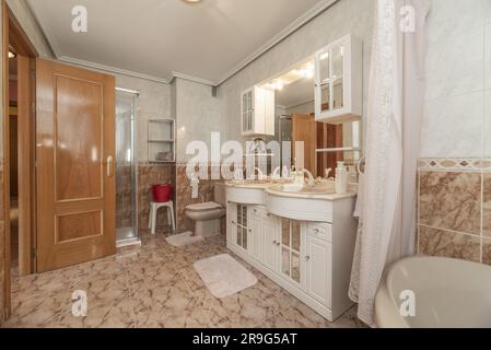 Konventionelle Toilette mit weißen Holzmöbeln mit zwei Porzellanschüsseln in der Marmorablage, Spiegel in den Möbeln und der Dusche Stockfoto