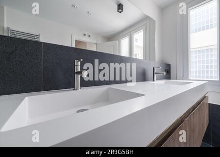 Bild eines wunderschönen, modernen Badezimmers mit einem langen Doppelwaschbecken, einem riesigen rahmenlosen Spiegel, dunklem Marmor und einem Schrank mit Holzboden und sauberem geradem Boden Stockfoto