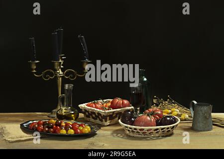 Stillleben mit verschiedenen Arten von leckeren reifen Tomaten, Kirschtomaten, Glasöldose, getrockneten Blumen und einem Kerzenhalter mit schwarzen Kerzen Stockfoto