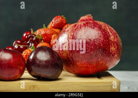 Stillleben mit reifem Granatapfel, roten Pflaumen und Beeren Stockfoto