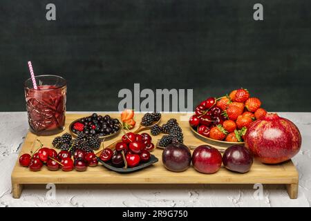 Stillleben von roten Beeren mit einem Glas Saft mit einem Strohhalm auf einer Bambusholzplatte Stockfoto