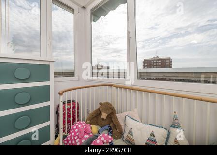 Ecke eines Kinderzimmers mit einem Kinderbett mit weißen Balken und Fenstern mit Aussicht Stockfoto