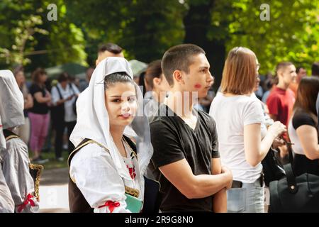 Bild eines stehenden Mädchens, das ein traditionelles serbisches Outfit in der Stadt Erdevik, Serbien trägt, neben einem jungen Mann mit einem Lippenstift-Fleck auf Hi Stockfoto