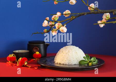 Teller mit leckerem chinesischen Reis, Teeset, Laternen und blühendem Ast auf farbigem Hintergrund Stockfoto