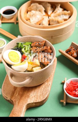 Kochtopf mit leckerer chinesischer Suppe und Jiaozi auf grünem Hintergrund Stockfoto