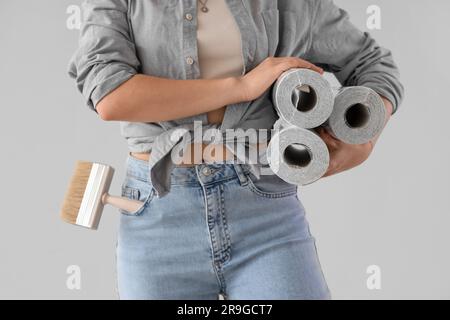 Junge Frau mit Tapetenrollen auf grauem Hintergrund, Nahaufnahme Stockfoto