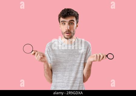Schockierter junger Mann mit Lupen auf pinkfarbenem Hintergrund Stockfoto