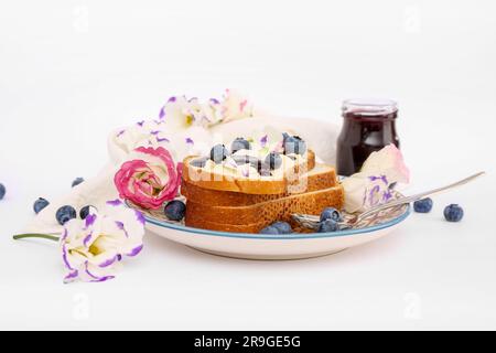 Teller mit köstlichen Marmeladentoasts, Blaubeeren und Blumen auf weißem Hintergrund Stockfoto