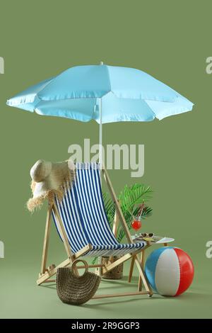 Komposition mit Liegestuhl, Sonnenschirm, Strandaccessoires und Cocktail auf dem Stuhl vor grünem Hintergrund. Reisekonzept Stockfoto