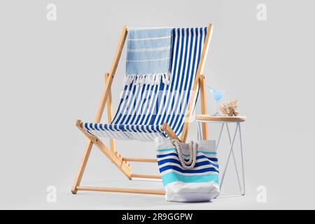 Liegestuhl mit Strandaccessoires, Cocktail und Korallen auf Hocker vor grauem Hintergrund Stockfoto