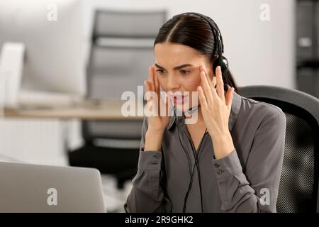 Gestresster Hotline-Mitarbeiter mit Headset, der im Büro auf einem Laptop arbeitet Stockfoto