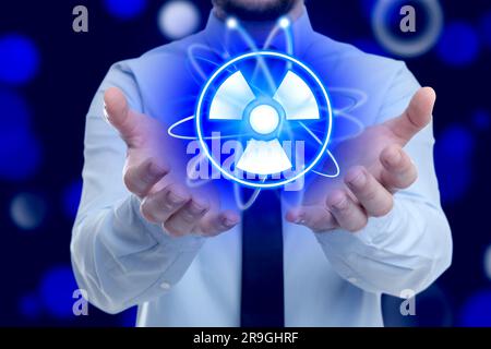 Mann mit Atom-Symbol und Strahlungswarnschild auf dunkelblauem Hintergrund, Nahaufnahme. Bokeh-Effekt Stockfoto