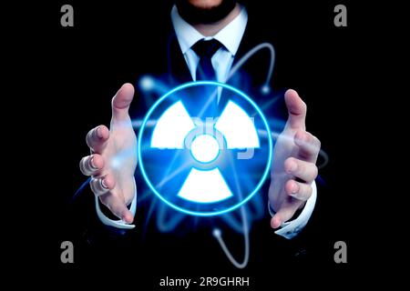 Mann mit leuchtendem Atom-Symbol und Strahlungswarnschild auf schwarzem Hintergrund, Nahaufnahme Stockfoto