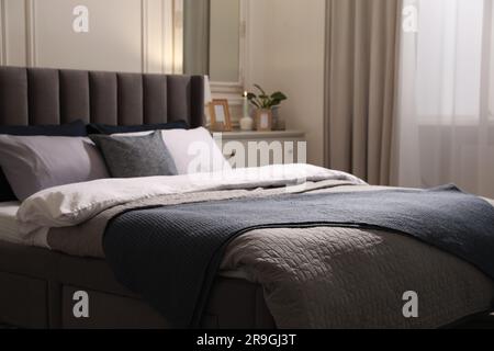 Komfortables Bett mit Kissen und Bettwäsche in stilvollem Zimmer. Innendesign Stockfoto