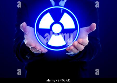 Mann mit leuchtendem Strahlungswarnsymbol auf dunkelblauem Hintergrund, Nahaufnahme Stockfoto