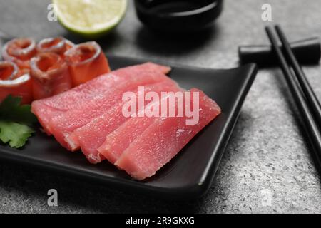 Sashimi-Set (roher Thunfisch und Lachs in Scheiben) mit Petersilie auf grauem Tisch, Nahaufnahme Stockfoto