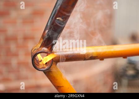 Manuelle Fahrradrenovierungsarbeiten, Lackentfernung durch Brennerfeuer, um die Farbe eines Fahrradrahmens zu ändern. Nahaufnahme. Stockfoto