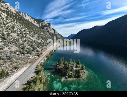 Ein Luftblick auf eine Straße, die sich durch eine Bergkette neben einer kleinen Insel in einem See schlängelt Stockfoto