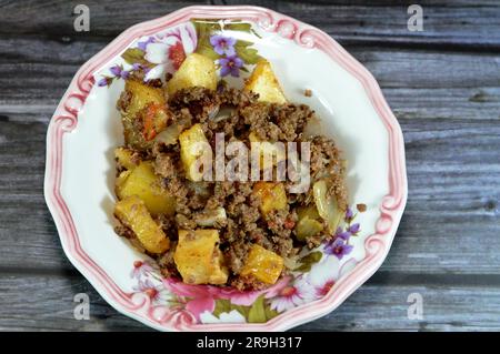 Ägyptische Küche mit gebratenen Kartoffelwürfeln, die dann mit Hackfleisch mit Öl, Knoblauch, Zwiebeln, Tomaten und Pfeffer gekocht werden, serviert auf einem auf Holz isolierten Teller Stockfoto