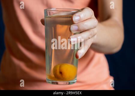 Ein Glas Kompott mit einer ganzen Aprikose unten in der Hand des Mädchens Stockfoto