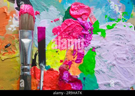 Abstrakter Hintergrund mehrfarbiger Farbe, auf dem der Pinsel und das Palettenmesser des Künstlers in Nahaufnahme dargestellt werden. Stockfoto