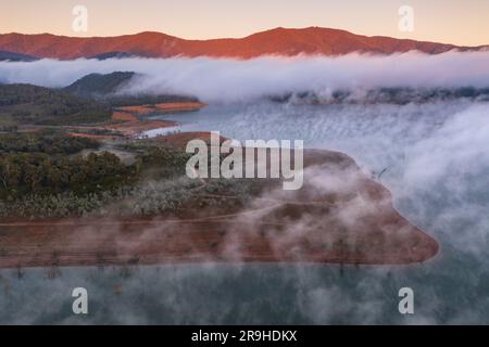 Der Nebel erhebt sich aus der Vogelperspektive von einem See mit Sonnenschein auf den nahegelegenen Hügeln am Lake Eildon in Victoria, Australien Stockfoto