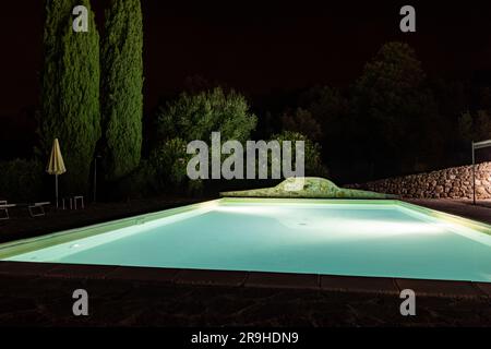 Beleuchteter Swimmingpool auf dem Hügel von Montemassi, umgeben von Zypressen und Oleandern in der Provinz Grosseto. Italien Stockfoto