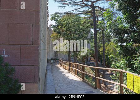 Gefliester Wanderweg im Freien entlang einer Festungsmauer und umgebende Bäume. Stockfoto