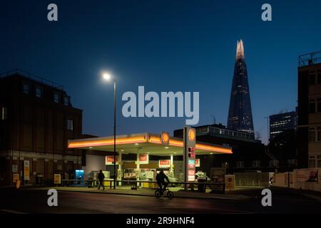 Das Wolkenkratzer-Gebäude von Shard hinter einer beleuchteten Shell Plc-Tankstelle bei Sonnenaufgang in London, Großbritannien Stockfoto