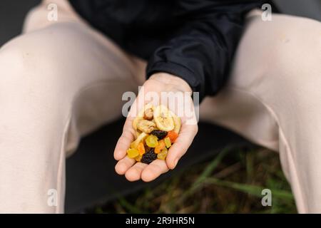 Verschiedene getrocknete Früchte, Nüsse in einer weiblichen Hand auf grünem Gras. Snack während der Wanderung, Spaziergang. Gesundes vegetarisches Essen. Stockfoto