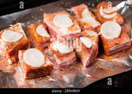 Rohe Schweineribs mit rohen Zwiebeln liegen auf Folie, fertig zum Backen im Ofen. Stockfoto