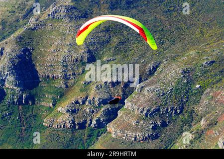 Gleitschirmfliegen vor der Vorderseite des Tafelbergs oder mit einem Stadtrand als Kulisse. Stockfoto