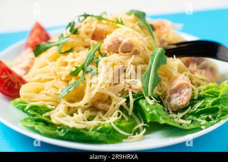 Spaghetti mit Lachs, Käse auf einem Salatsalat, bestreut mit Rucola und Kirschtomaten aus nächster Nähe Stockfoto