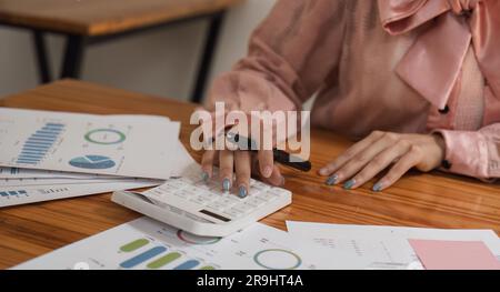 Nahaufnahme der Hände einer Geschäftsfrau mit einem Taschenrechner, um die Finanzen und Einnahmen des Unternehmens sowie das Budget zu prüfen. Geschäftsfrau, die die monatlichen Ausgaben berechnet Stockfoto
