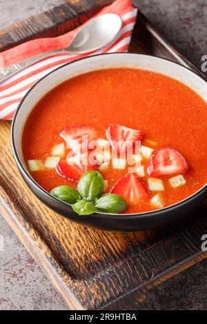 Sommergazpacho-Suppe mit Erdbeeren, Tomaten, Gurken und Basilikum in einer Schüssel auf dem Tisch. Vertikal Stockfoto