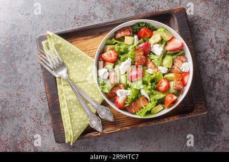 Hausgemachter, frischer Salat mit Erdbeeren, Avocado, Speck, Salat, Fetakäse in einer Schüssel auf dem Tisch. Horizontale Draufsicht von oben Stockfoto