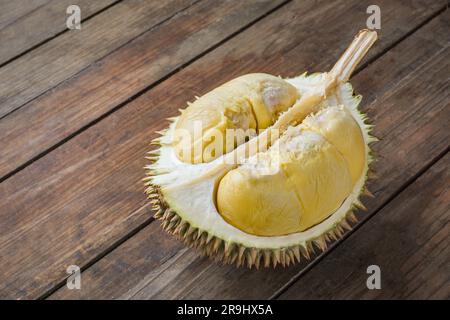 Auf einem Holztisch in zwei Hälften geschnittene Durianfrüchte. Die Durianfrucht ist die essbare Frucht mehrerer Baumarten der Gattung Durio. Stockfoto