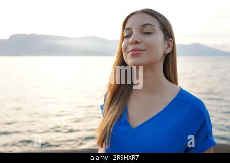 Attraktive junge Frau atmet mit geschlossenen Augen auf die Sonnenuntergangslandschaft Stockfoto