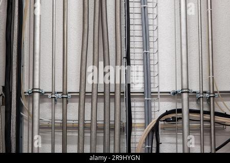 Vertikale, wandmontierte Rohre und elektrische Kabel in einer industriellen Umgebung. Vorderansicht, keine Leute. Stockfoto