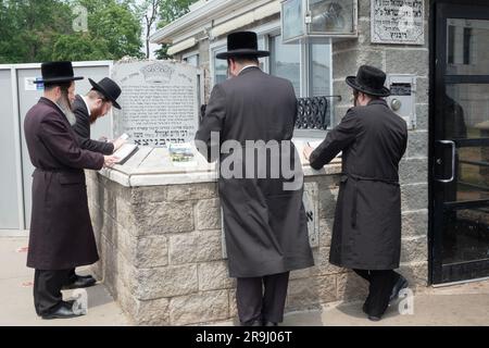 Vier jüdische Männer beten am Grabstein des Ribnitz Rebbe, da man annimmt, dass Gebete in der Nähe der Gerechten verstärkt werden. In Monsey New York. Stockfoto