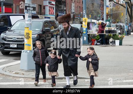 Während des Passover geht ein chassidischer jüdischer Mann mit traditionellem Shtreimel-Pelzhut mit seinen Kindern in Brooklyn, New York, spazieren. Stockfoto