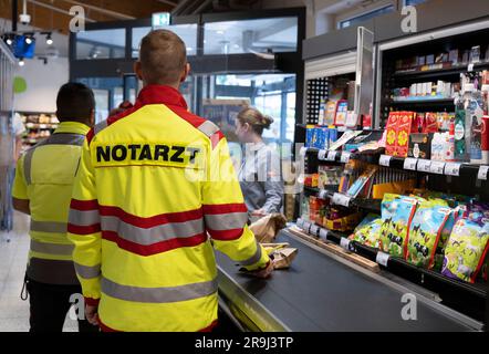 27. Juni 2023, Hessen, Brachttal: Ein Notarzt steht an einem Supermarkt-Checkout (Pose Scene). Die Kampagne „Emergency Lane at the Checkout“ im Bezirk Main-Kinzig soll die Abwicklung von Notdiensten an der Kasse in der Zukunft beschleunigen. Foto: Boris Roessler/dpa Stockfoto