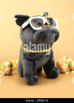 Weiches, weiches, schwarzes Hundetier mit goldener Sonnenbrille und glänzenden goldenen Weihnachtskugeln auf goldenem Hintergrund. Vertikale Fotografie, Vorderansicht. Stockfoto