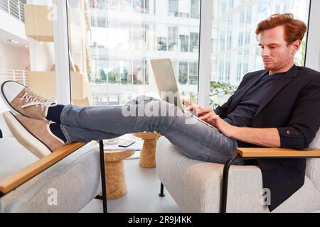 Entspannter Geschäftsmann, der mit dem Laptop sitzt, während er mit den Füßen auf dem Stuhl sitzt Stockfoto