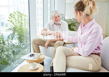 Geschäftsfrau schüttelt dem älteren Geschäftsmann in der Lounge die Hand Stockfoto