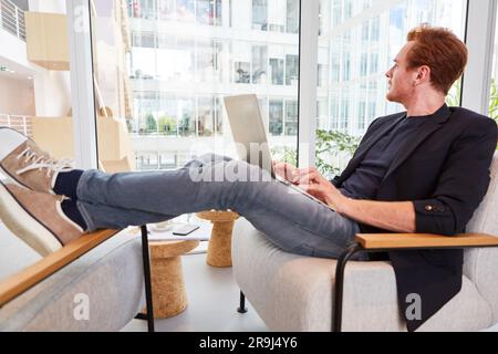 Aufmerksamer Geschäftsmann, der mit dem Laptop sitzt, während er mit den Füßen auf dem Stuhl sitzt Stockfoto
